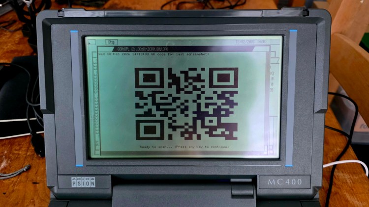 A close-up of a Psion MC400 device displaying a QR code on its screen, with text indicating it's ready to scan.