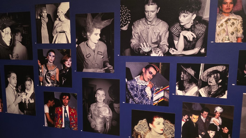 A collage of black and white photos showcasing various individuals in artistic costumes and expressive styles, set against a blue wall.
