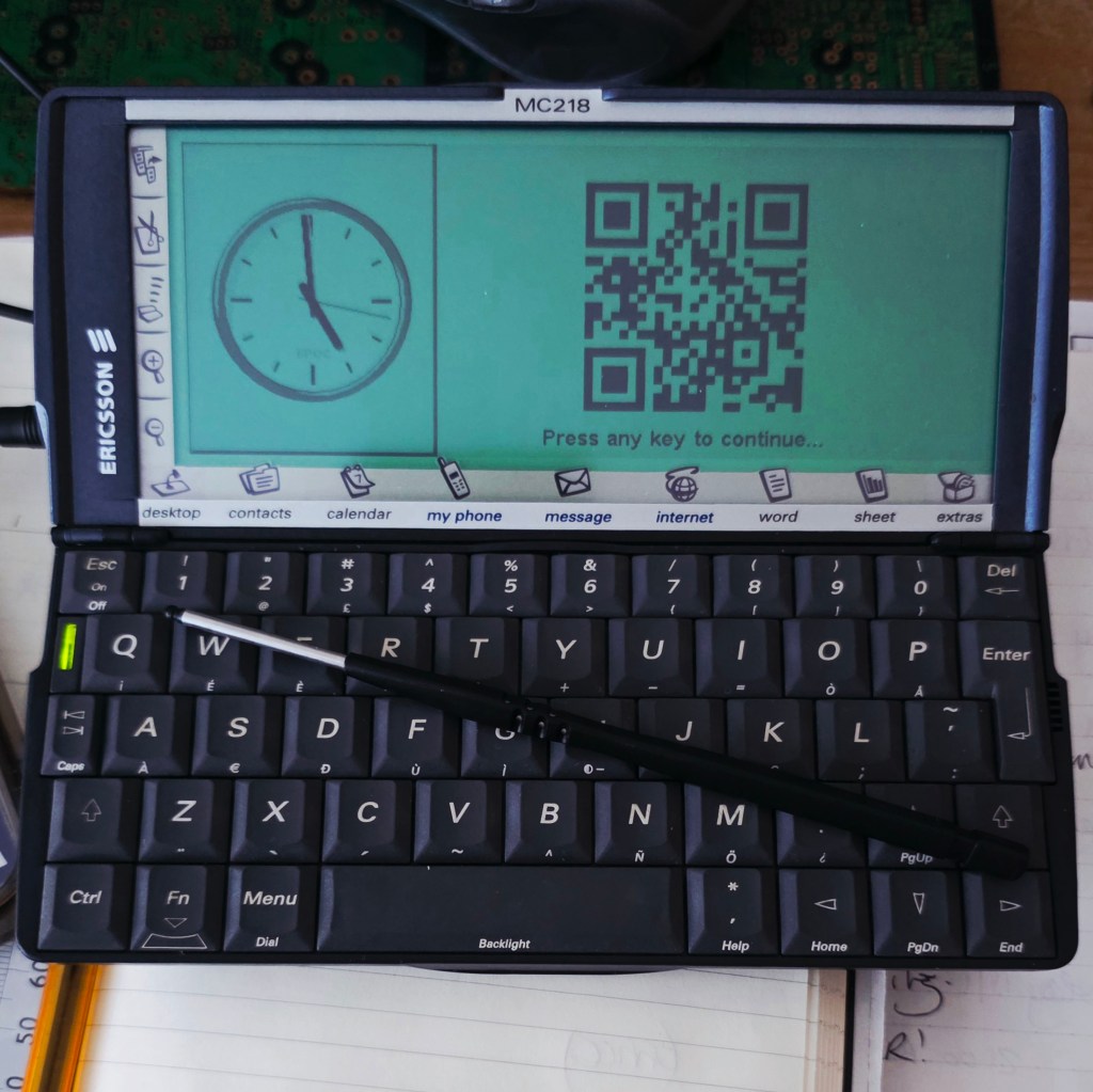 An Ericsson MC218 device displaying a clock and a QR code on its screen, with a black stylus resting on its keyboard.