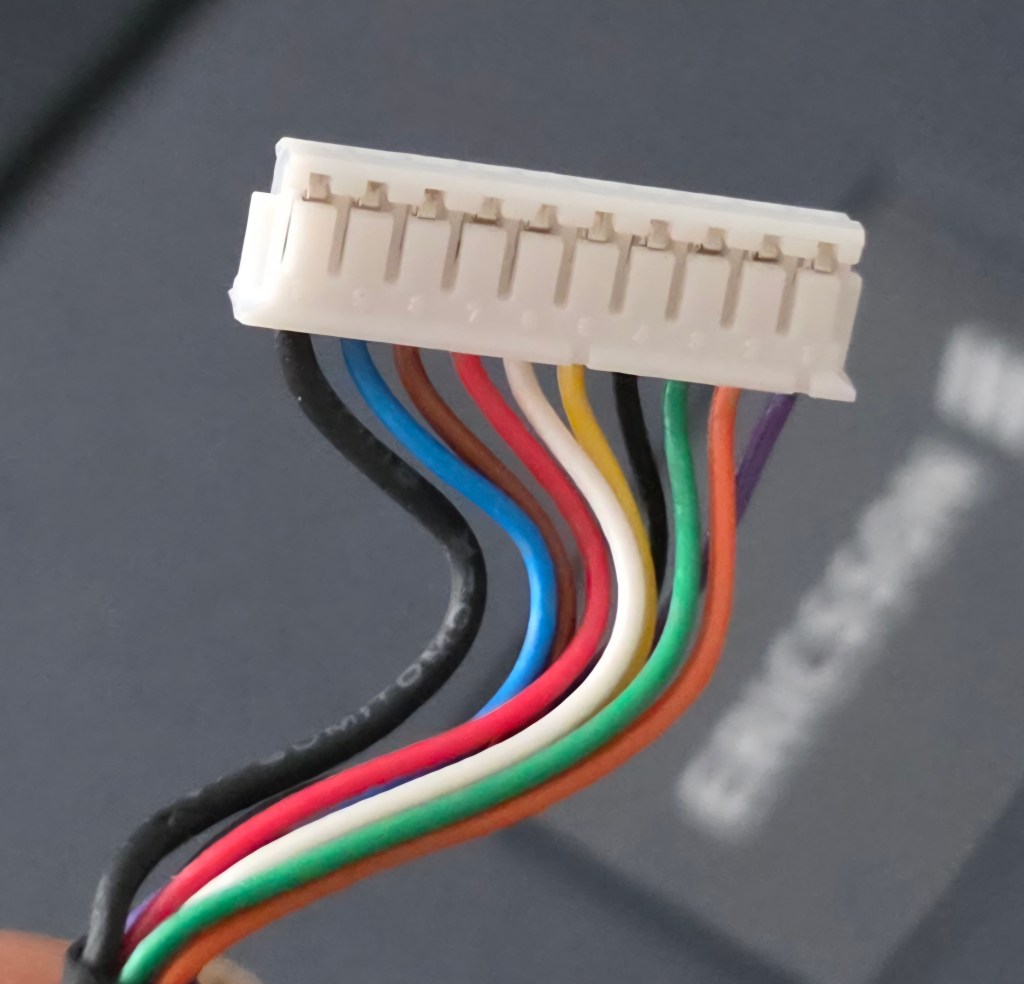 Close-up of a multi-colored electrical connector with multiple wires attached, featuring a white plastic housing.