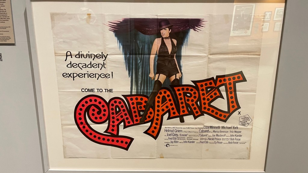 A vintage poster for the musical 'Cabaret' featuring a woman in a black outfit and hat, with the text 'A divinely decadent experience! Come to the CABARET' in bold colorful letters.
