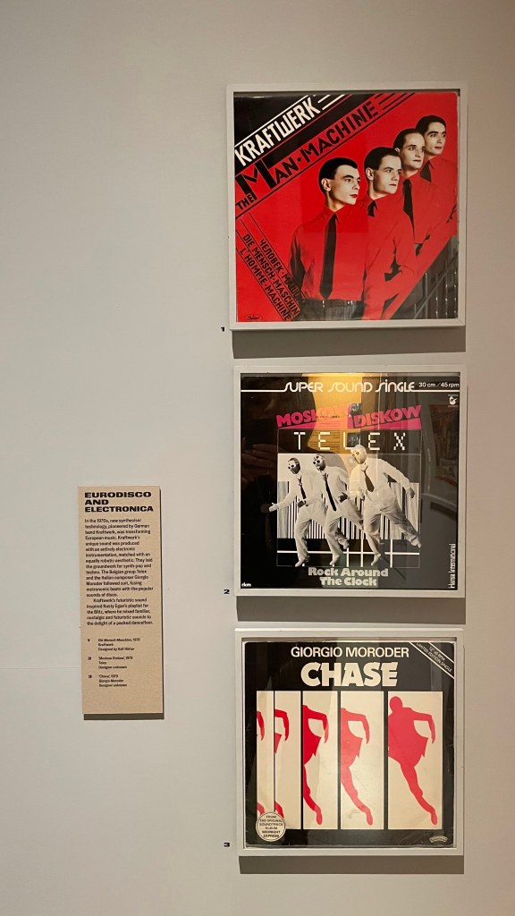 Three framed album covers displayed on a wall, including 'The Man-Machine' by Kraftwerk, 'Rock Around The Clock' by Telex, and 'Chase' by Giorgio Moroder.